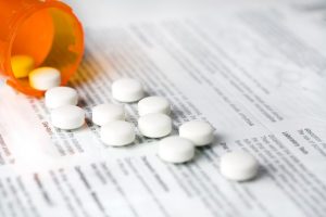 white pills spilling from vial onto drug information sheet