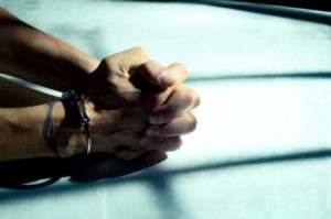 male cuffed hands over dirty white table lit through the cell bars with harsh light