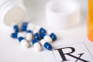 blue-and-white capsules spilling from a prescription medicine bottle across the corner of a prescription; shallow depth-of-field image with focus on the nearest capsule